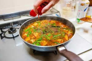 グツグツと火にかけたフライパンの中の麻婆豆腐にラー油を垂らす　イメージ画像